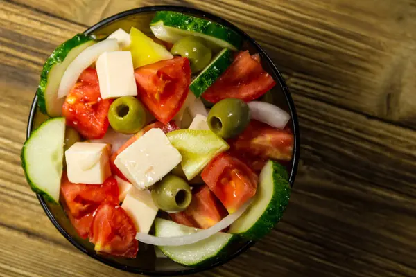 Греческий салат в стеклянной чаше на деревянном столе — стоковое фото