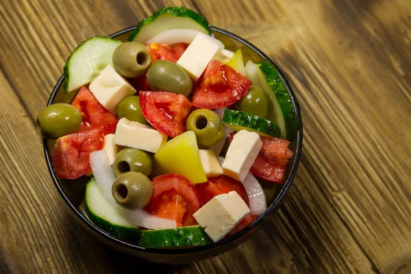 Греческий салат в стеклянной чаше на деревянном столе — стоковое фото