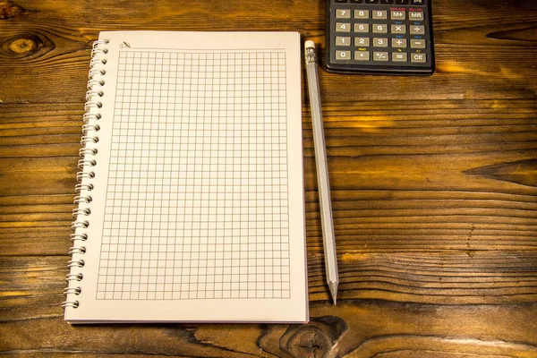 Bloco de notas com lápis e calculadora na mesa de madeira — Fotografia de Stock