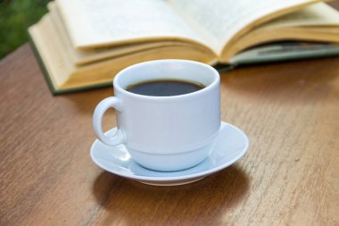 Bir fincan kahve ve kitap ahşap masada.