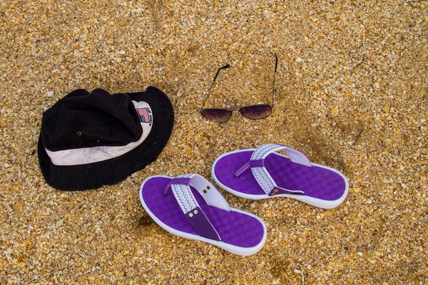 Пара шлепанцев, шляпа и солнцезащитные очки на песчаном пляже — стоковое фото