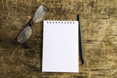 Not Defteri, gözlük ve kalem eski ahşap masa üzerinde. Üstten Görünüm