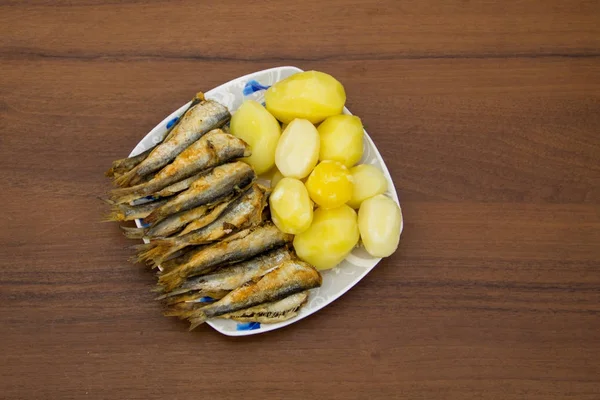 Fried baltic herring with boiled potatoes on a plate on wooden table — Stock Photo, Image