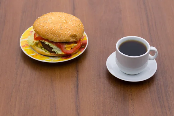 Herkullinen hampurilainen ja kuppi kahvia puupöydällä — kuvapankkivalokuva