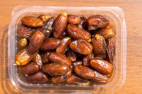 Dried date fruits in plastic container on wooden table. Top view — Stock Photo, Image