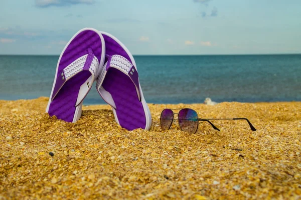 Par de chinelos e óculos de sol em uma praia de areia — Fotografia de Stock