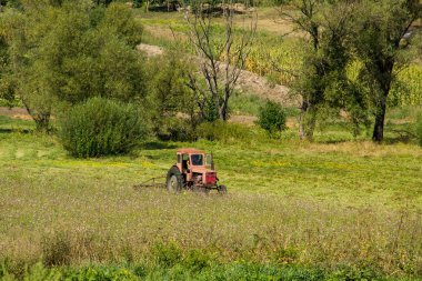Yaşlı kırmızı traktör çayırda haykırıyor.