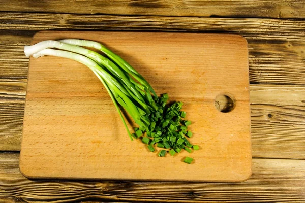 Chopped green onions on cutting board on wooden table. Top view — Stock Photo, Image