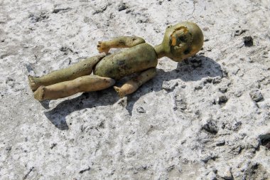 Gri beton zeminde terk edilmiş kırık bir oyuncak bebek.