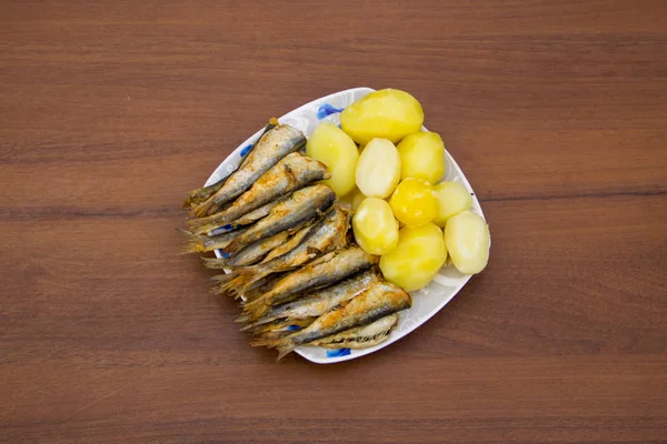 Gebakken Oostzeeharing gekookte aardappelen op een bord op de houten tafel — Stockfoto