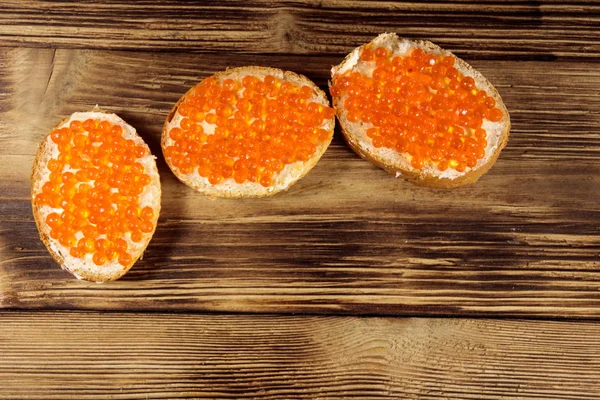 Sanduíches com manteiga e caviar vermelho na mesa de madeira — Fotografia de Stock