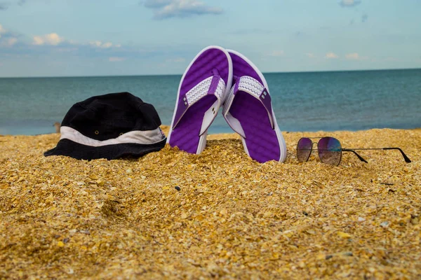 Ζευγάρι σαγιονάρες, καπέλο και γυαλιά ηλίου στην αμμώδη παραλία — Φωτογραφία Αρχείου