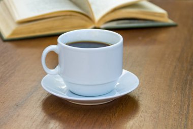 Bir fincan kahve ve kitap ahşap masada.