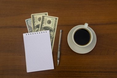 Fincan kahve, dolar, not defteri ve kalem ahşap masa