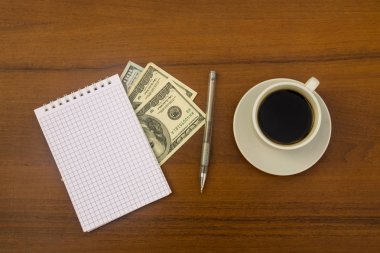 Fincan kahve, dolar, not defteri ve kalem ahşap masa