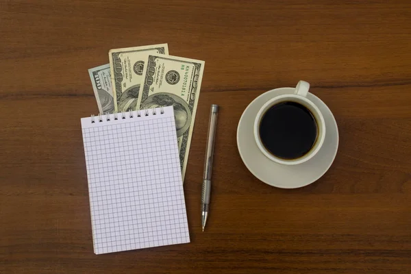 Fincan kahve, dolar, not defteri ve kalem ahşap masa