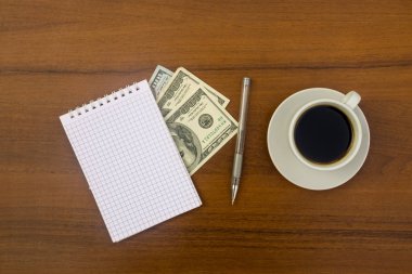 Fincan kahve, dolar, not defteri ve kalem ahşap masa