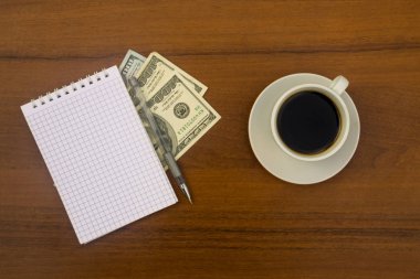 Fincan kahve, dolar, not defteri ve kalem ahşap masa