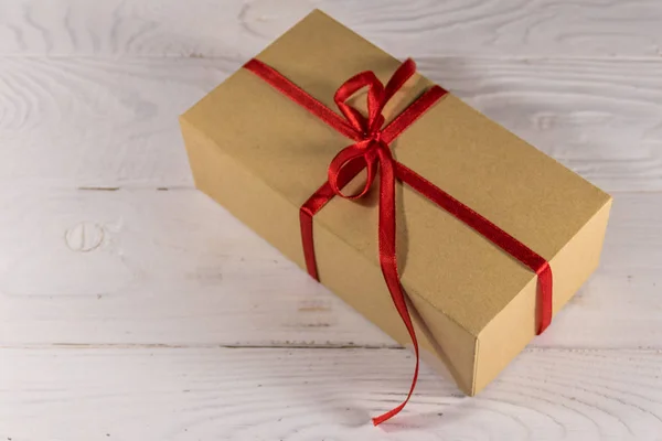 Kartonnen geschenkdoos met rood lint op witte houten tafel — Stockfoto