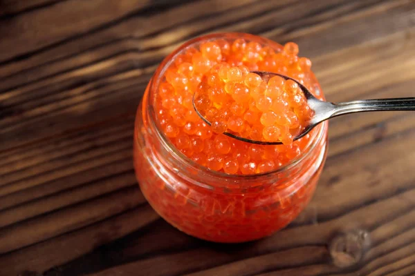 Caviar vermelho em frasco de vidro na mesa de madeira — Fotografia de Stock
