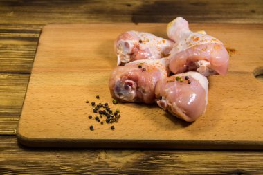 Çiğ tavuk bacağı ve ahşap masada baharatlar.