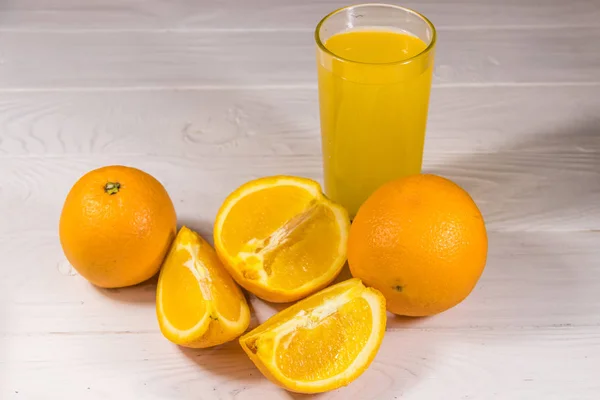 Glass of orange juice and fresh oranges on white wooden table — Stock Photo, Image