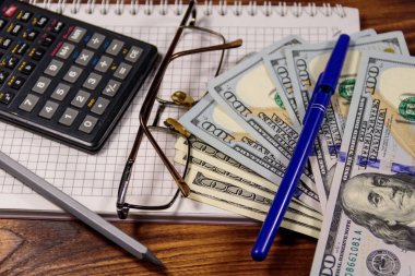 Defter ile dolar, kalem, gözlük ve ahşap masa hesap makinesi