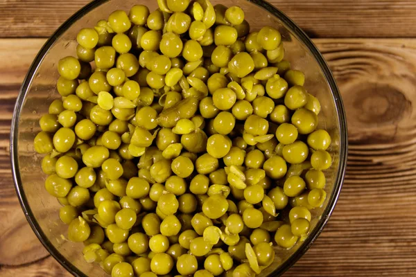 Ingeblikte groene erwten in glazen kom op houten tafel — Stockfoto