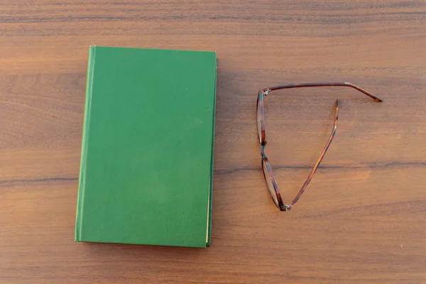 Livro fechado e óculos em fundo de madeira — Fotografia de Stock