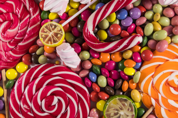Background of colorful chocolate candies, lollipops, candy cane and marshmallows