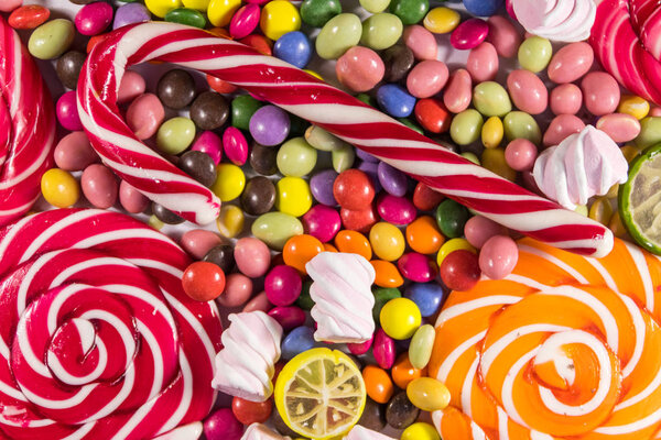 Background of colorful chocolate candies, lollipops, candy cane and marshmallows