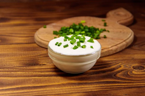 Saure Sahne und grüne Zwiebeln auf Holztisch — Stockfoto