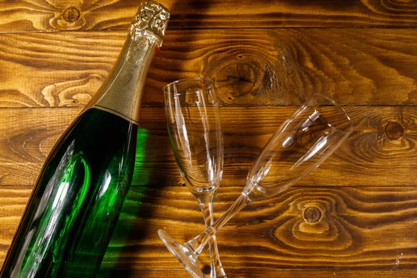 Láhev šampaňského a dvě prázdné sklenice šampaňského na dřevěném pozadí. Horní pohled — Stock fotografie