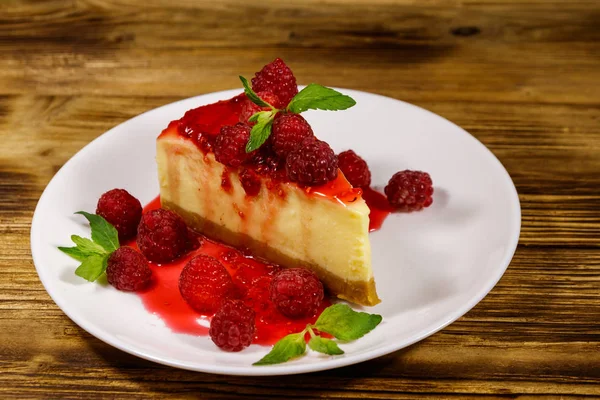 Leckeres Stück New Yorker Käsekuchen mit Himbeeren und Himbeermarmelade in einem weißen Teller auf einem Holztisch — Stockfoto