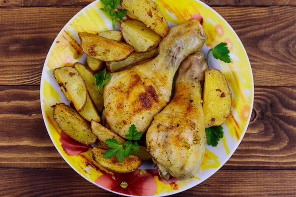 Gebakken kip drumsticks met aardappelen in een bord op houten tafel — Stockfoto