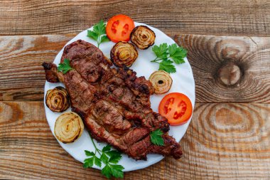 Izgara domuz etli soğan, domates ve maydanoz ahşap masa üzerinde beyaz plaka 