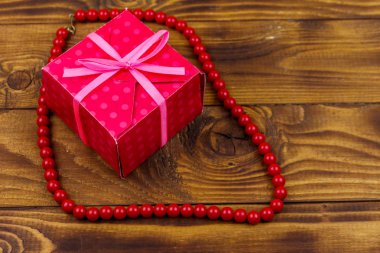 Ahşap arka plan üzerinde hediye kutusu ve kırmızı boncuk kolye