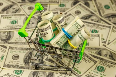 Amerika 'nın arka planında 100 dolarlık banknotlarla dolu küçük bir alışveriş arabası. Tüketici kavramı