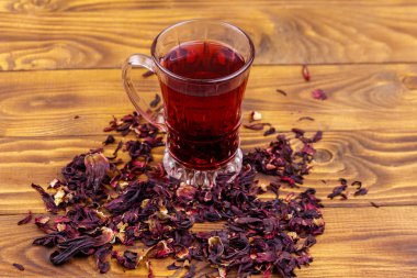 Ahşap masada bir bardak kırmızı amber çayı (carcade, roselle).