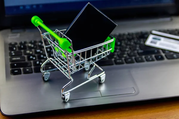 Concepto de compras online. Pequeño carrito de compras con caja y tarjeta de crédito en el teclado portátil —  Fotos de Stock