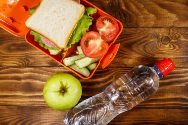 Sandviç ve taze sebze, su şişesi ve ahşap masa üzerinde yeşil elma ile Okul öğle yemeği kutusu. Sağlıklı beslenme konsepti. Üstte görüntü
