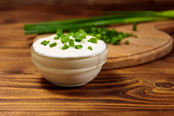 Saure Sahne und grüne Zwiebeln auf Holztisch — Stockfoto