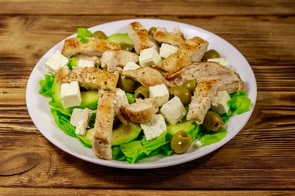 Tasty salad with fried chicken breast, green olives, feta cheese, avocado, lettuce and olive oil on wooden table — Stock Photo, Image