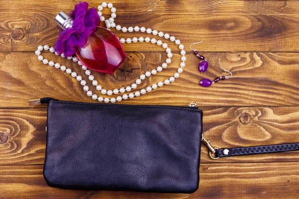 Women accessories on wooden background. Clutch bag, bottle of perfume, pearl necklace and earrings on wood table. Beauty and fashion composition. Top view, flat lay