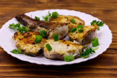 Ahşap bir masada beyaz tabakta kavrulmuş pollock.