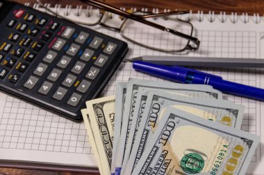 Defter ile dolar, kalem, gözlük ve ahşap masa hesap makinesi