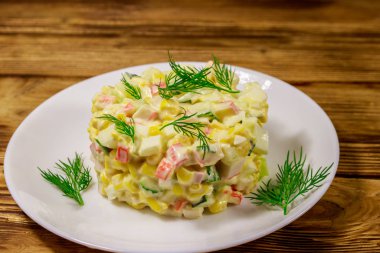 Yengeç çubuklu salata, tatlı mısır, salatalık, yumurta ve mayonez ahşap masada.