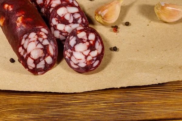 Sliced salami sausage on brown paper on wooden table — Stock Photo, Image