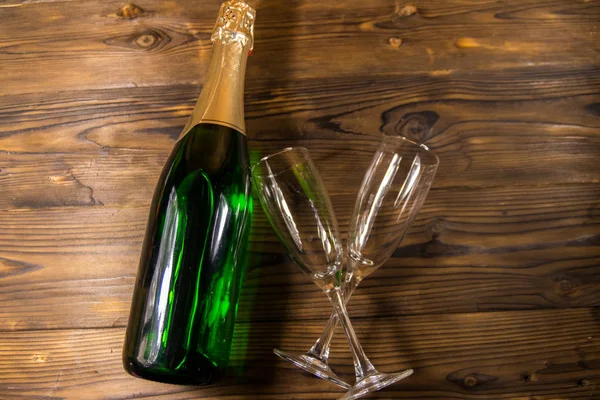 Láhev šampaňského a dvě prázdné sklenice šampaňského na dřevěném pozadí. Horní pohled — Stock fotografie