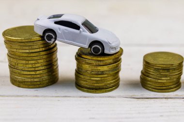 Beyaz ahşap arka plan üzerinde altın sikke yığınları üzerinde Minyatür araba modeli